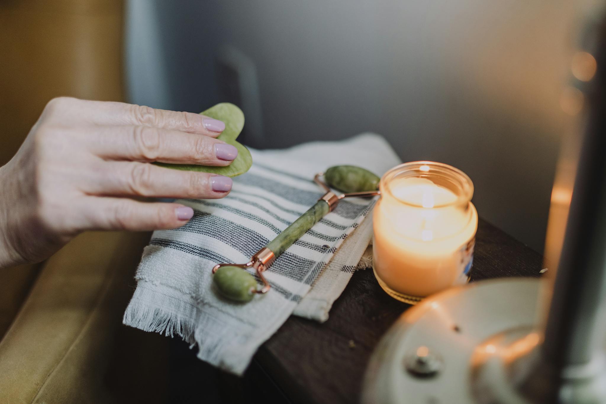 A calming self-care setup featuring a jade roller, candle, and cozy ambiance, perfect for relaxation.