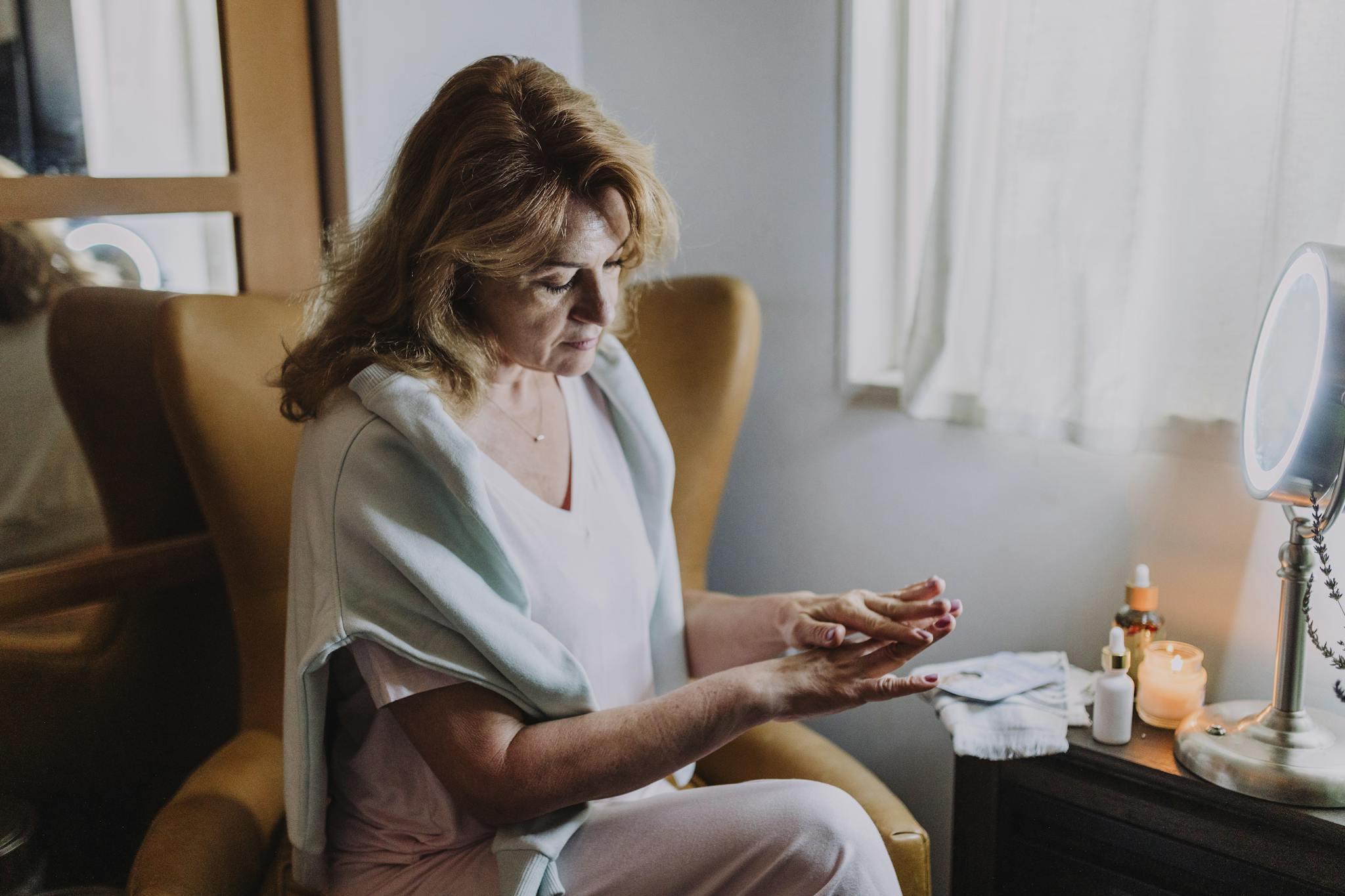 An adult woman enjoys a relaxing home spa day, applying skincare products by the window.