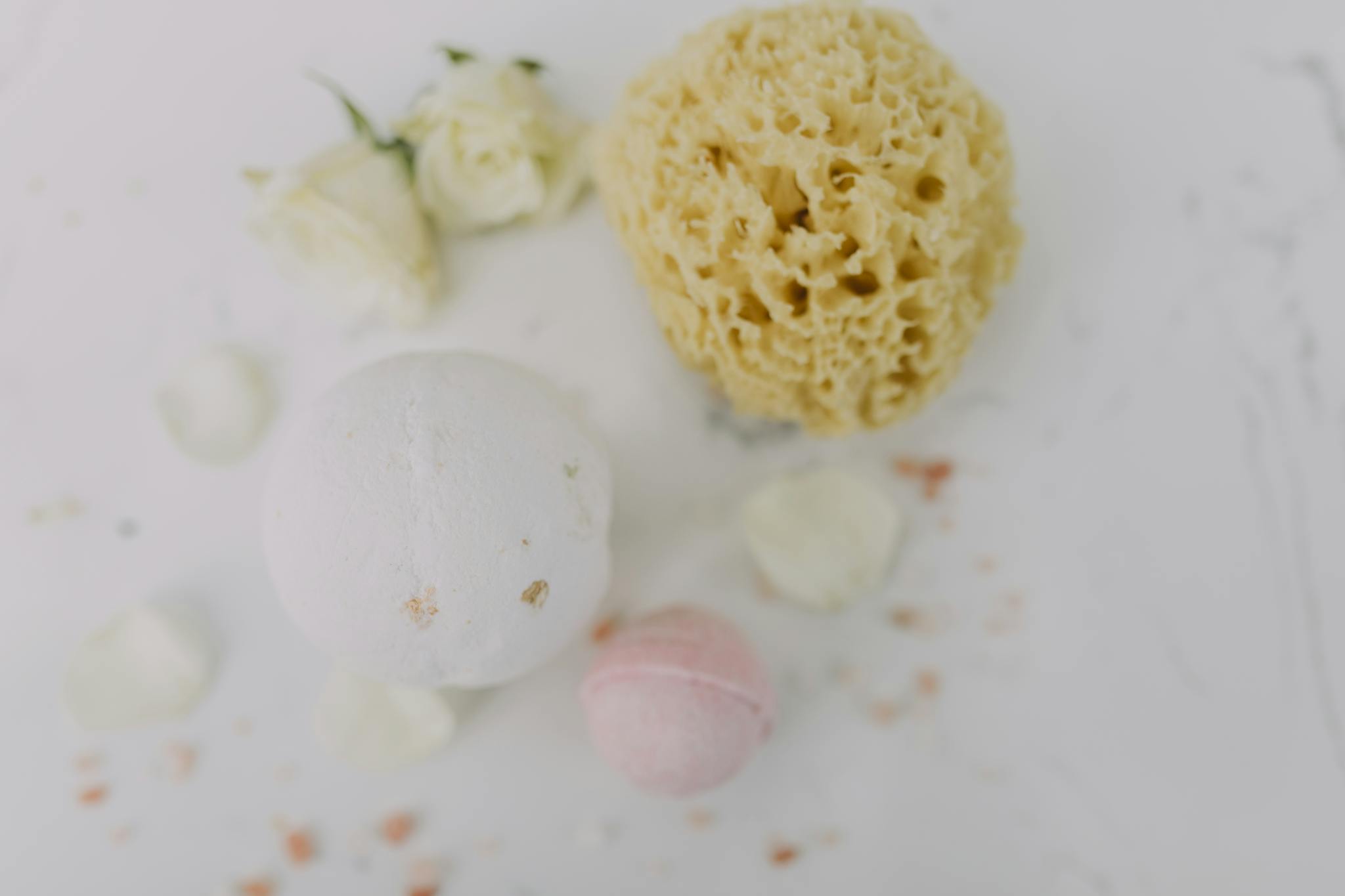 Flat lay of spa essentials featuring bath bombs, sponge, and rose petals for a relaxing experience.